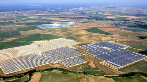 Aerial view of the unit I, III, and IV, of Abengoa Solar's Solnova Solar Power Station. The two towers and reflective mirrors in the background are the PS10 and PS20 solar power plants, also owned by Abengoa Solar. This region is also sometimes known as the Solar Platform.