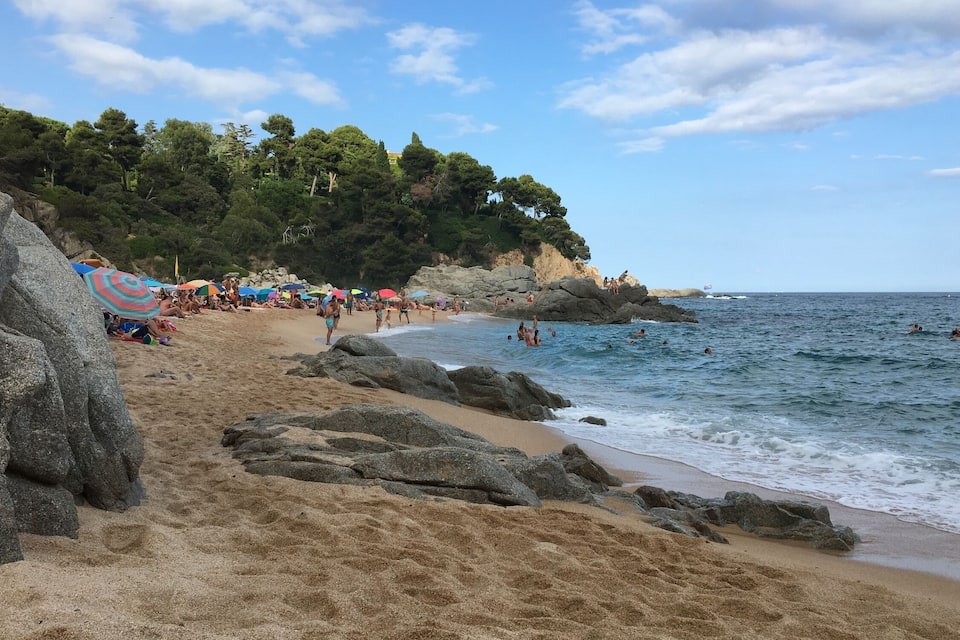 Ein Strand mit Menschen, die sonnenbaden, schwimmen und am Ufer entlanggehen.