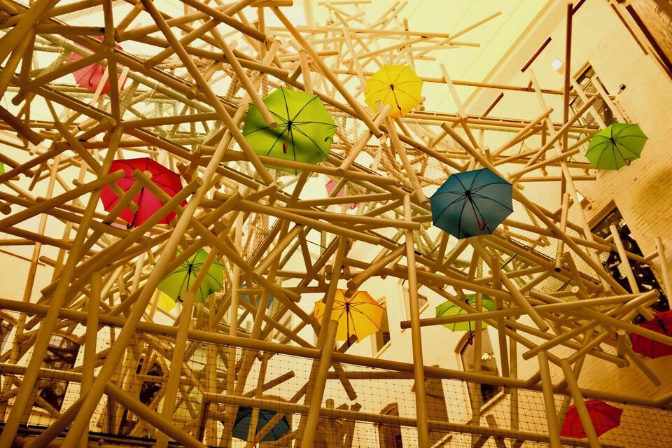 Una estructura complexa de bigues metàl·liques blanques amb ombrelles de colors penjades.