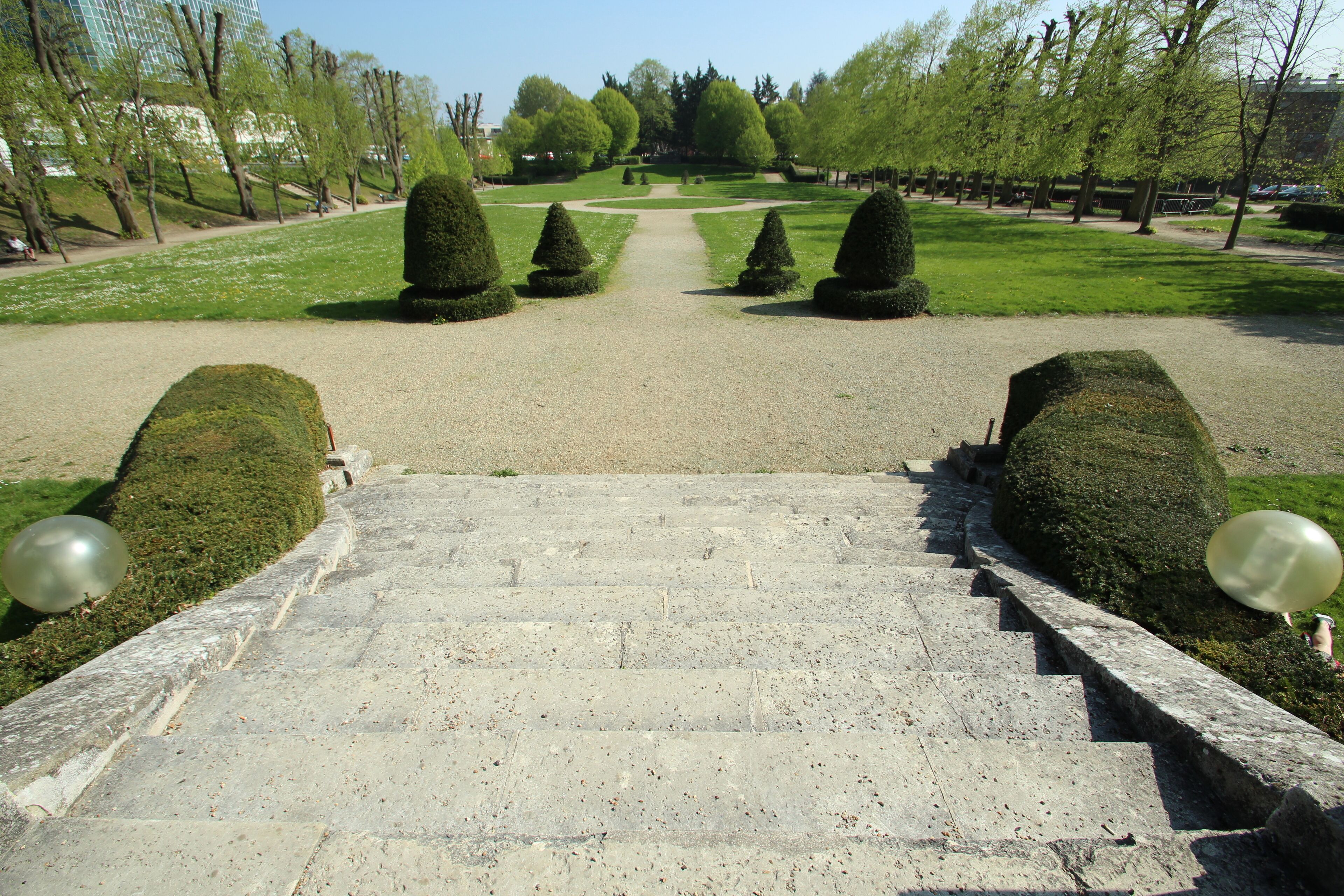 A stone staircase leading to a park with neatly trimmed trees and a clear sky.
