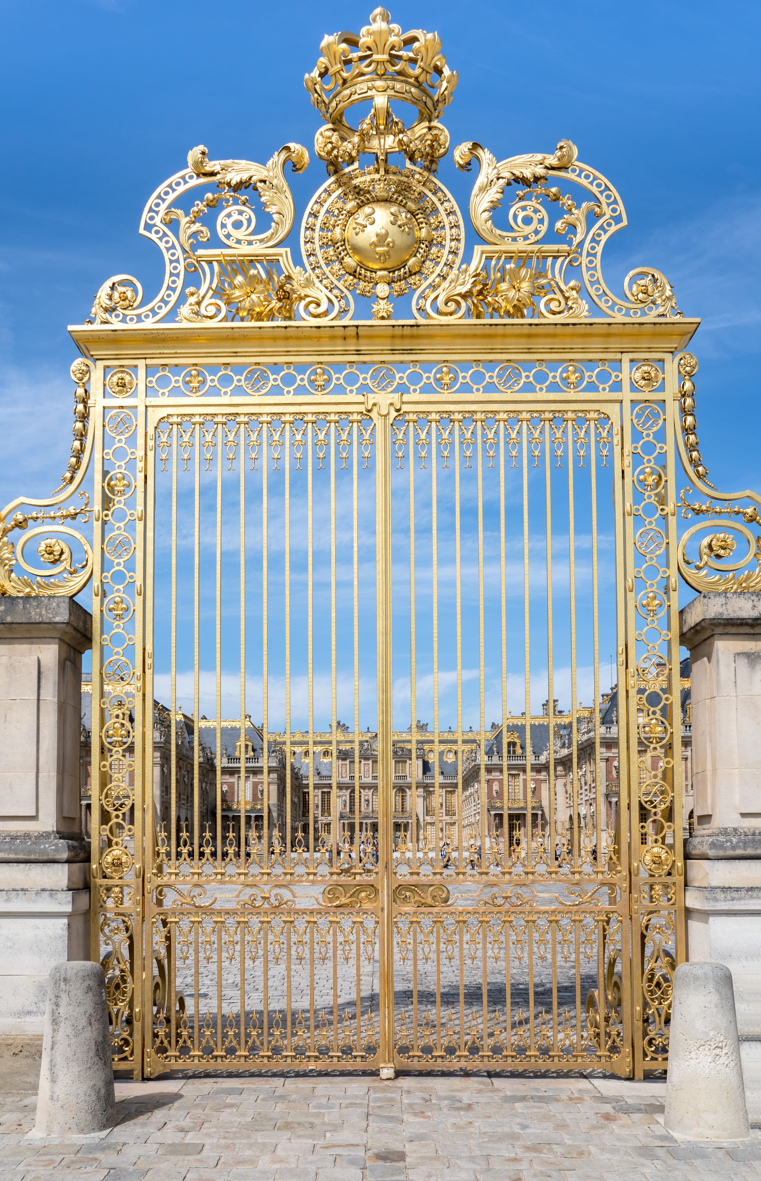 Un cancello dorato e decorato, con listelli verticali e motivi intricati, sullo sfondo di un cielo azzurro intenso.