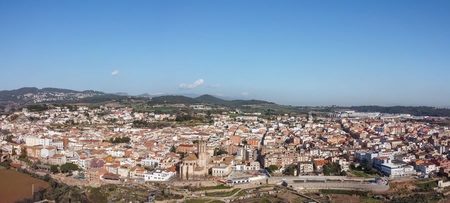 Vista panorámica de una ciudad costera con una catedral destacada, un área urbana densa y colinas circundantes.