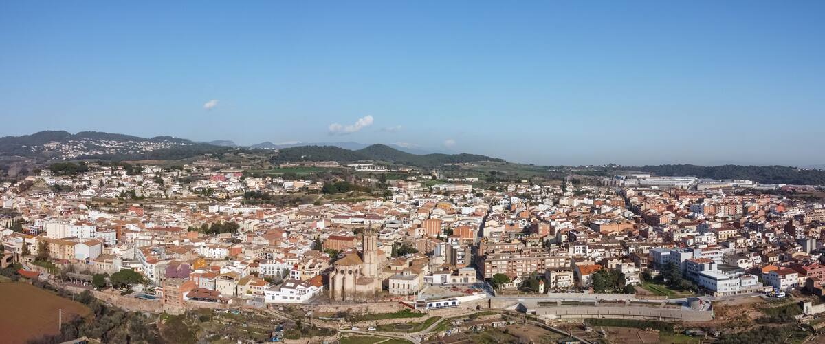 A panoramic view of a coastal city with a prominent cathedral, dense urban area, and surrounding hills.