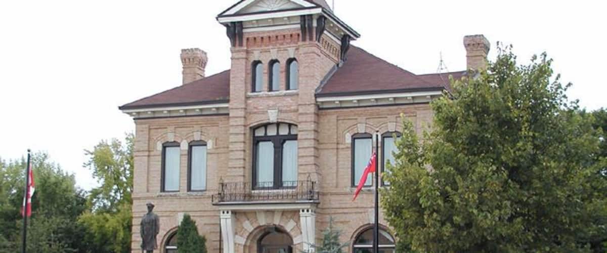 A historic brick building with a prominent entrance, a statue, and a flagpole.