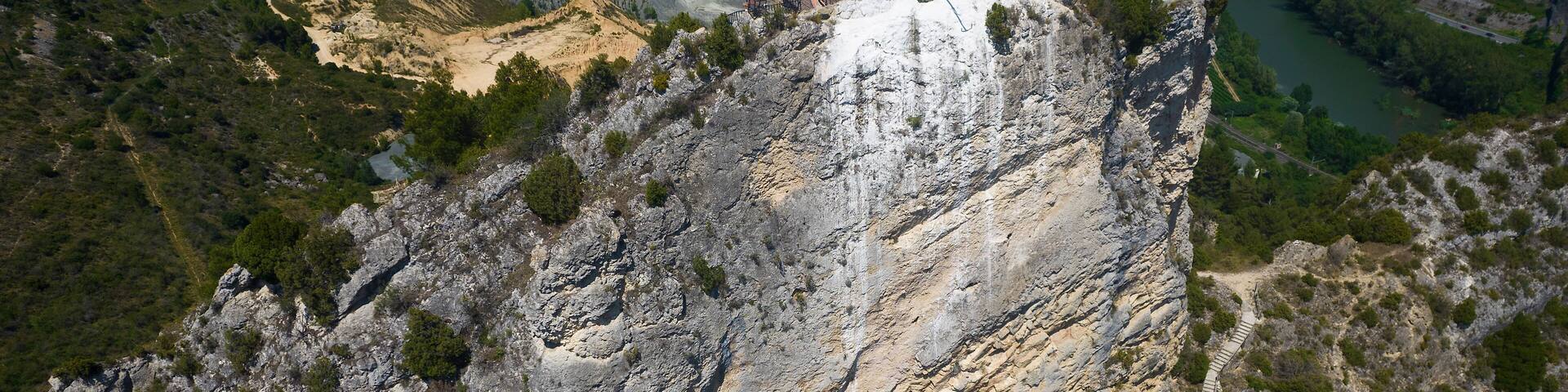 A rocky cliff with a statue on top, a river below, and a distant town.