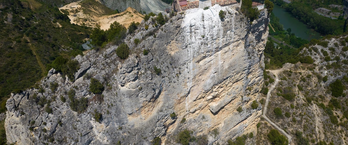 A rocky cliff with a statue on top, a river below, and a distant town.