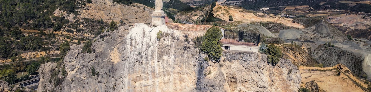 Une montagne rocheuse surmontée d’une statue, entourée d’une vallée et de collines lointaines.