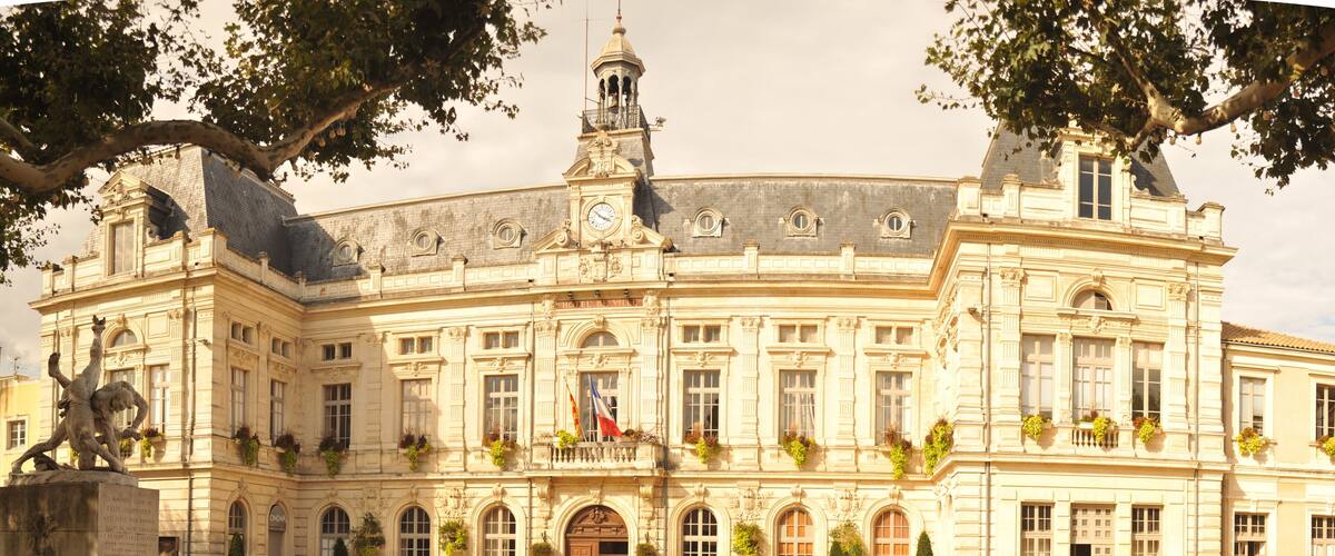 A grand historic building with a clock tower, statues, and flags.