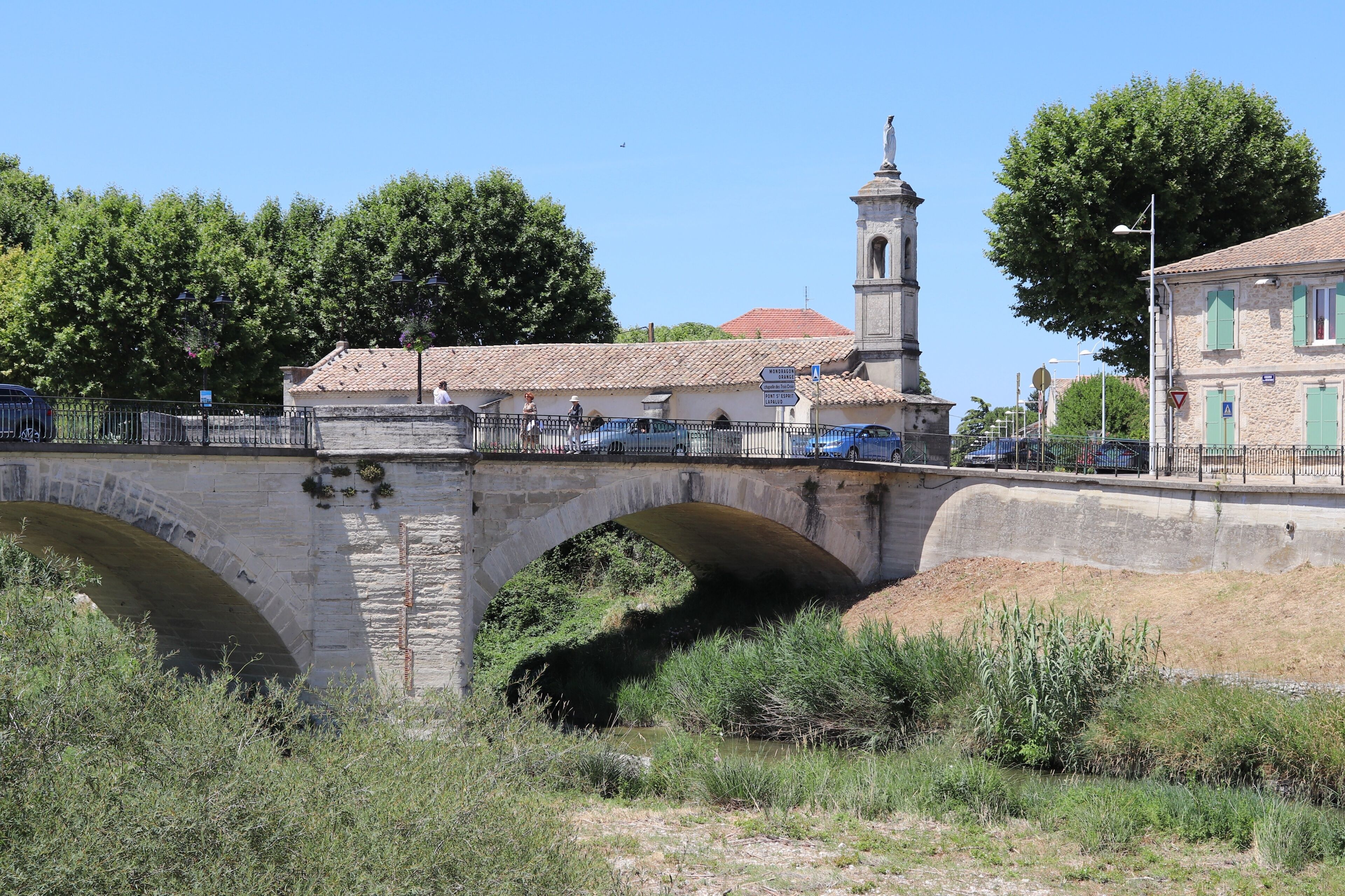 A stone bridge with arches, a church with a bell tower, and a clear blue sky.