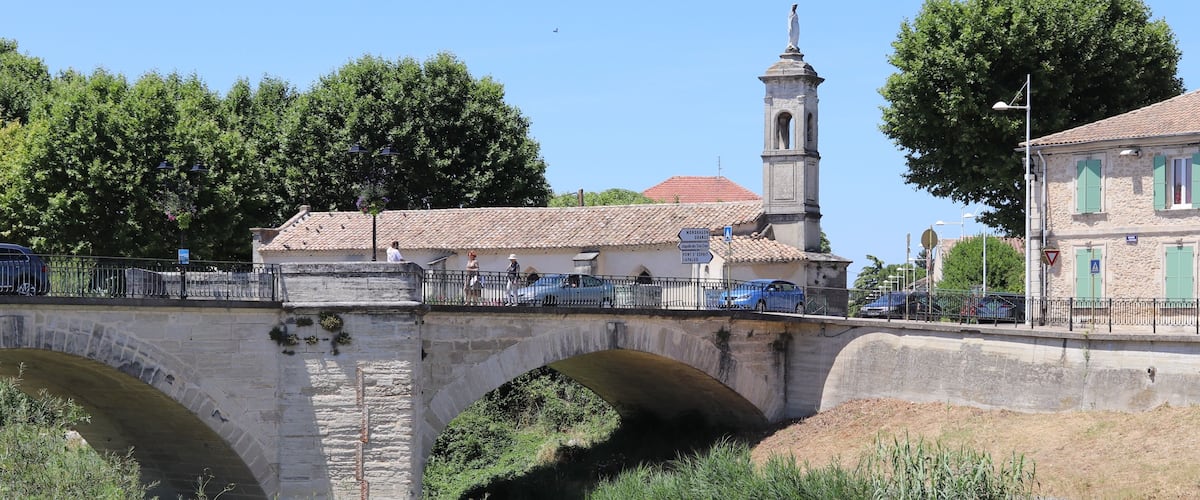 Un pont de pierre à arcades, une église dotée d’un clocher et un ciel d’un bleu limpide.