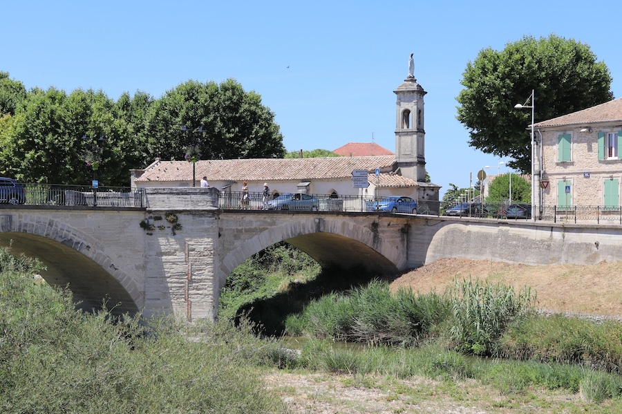 A stone bridge with arches, a church with a bell tower, and a clear blue sky.