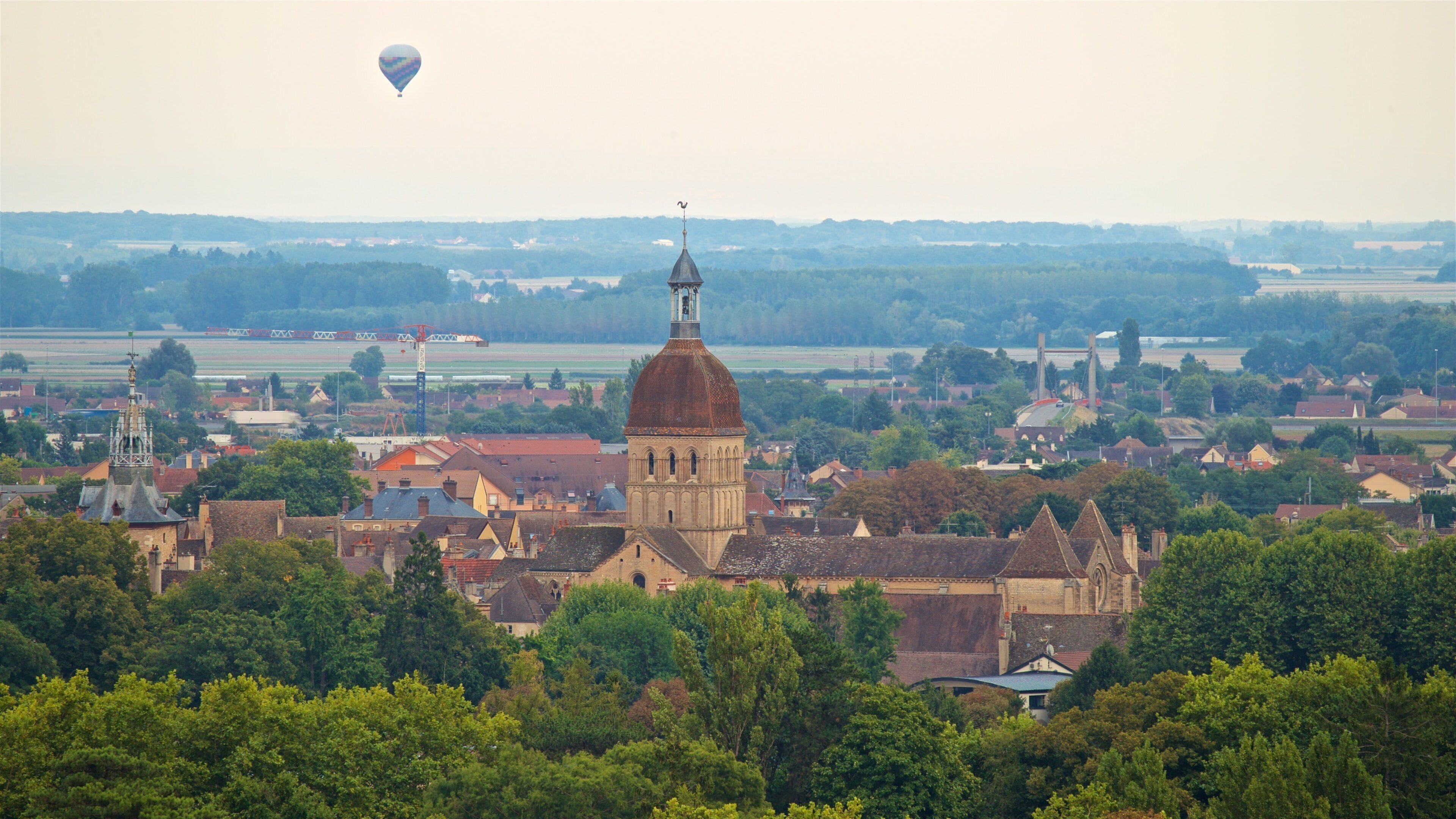 A town with a prominent church tower, lush greenery, and a hot air balloon in the sky.