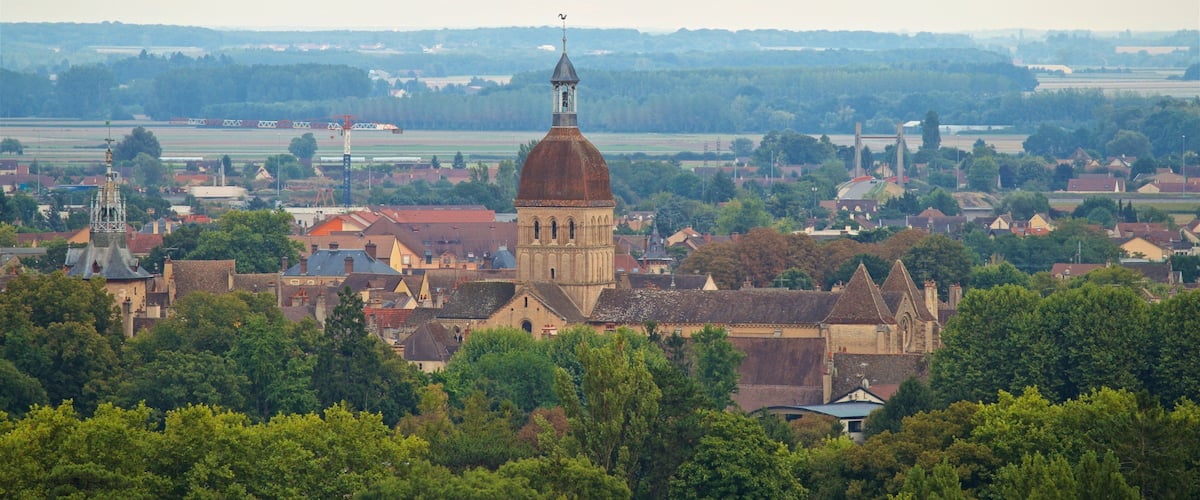 A town with a prominent church tower, lush greenery, and a hot air balloon in the sky.
