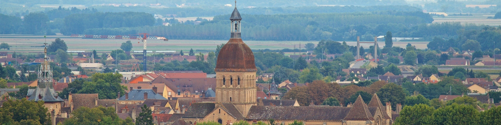 Uma cidade com uma torre de igreja imponente, vegetação exuberante e um balão de ar quente no céu.