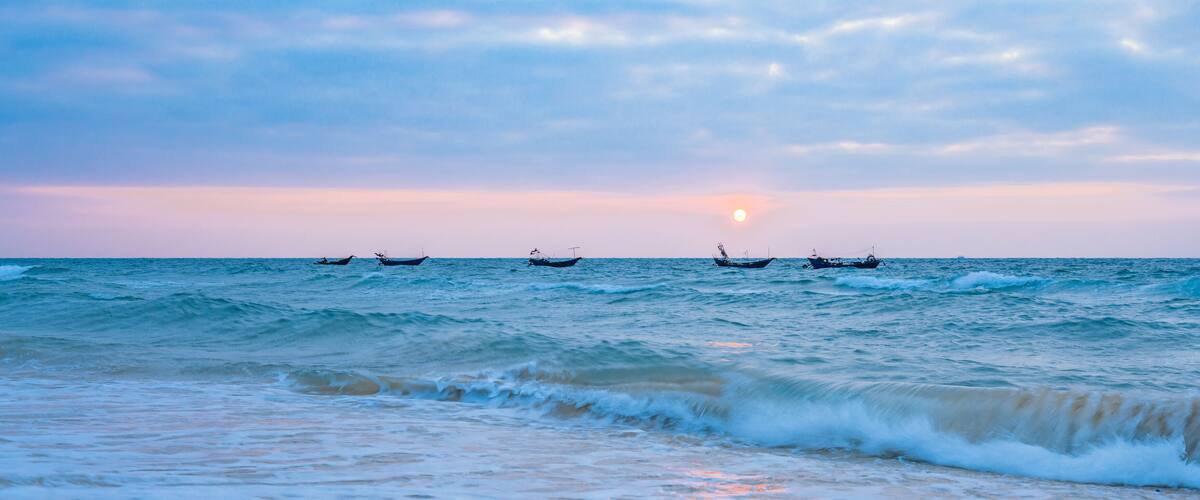 A sunset over the ocean with several boats.