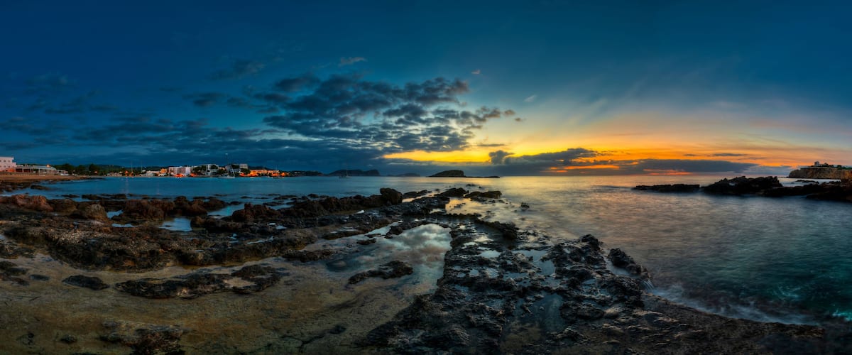 A coastal landscape with rocky shores, calm water, and a sunset sky.