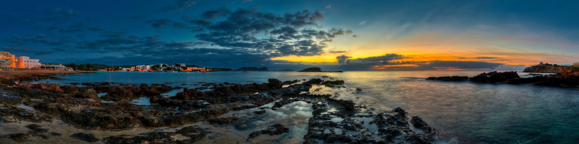 A coastal landscape with rocky shores, calm water, and a sunset sky.