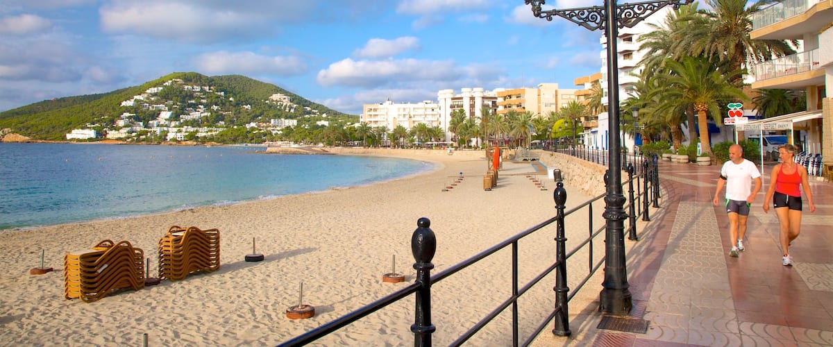 A beach with a promenade, palm trees, and buildings in the background.