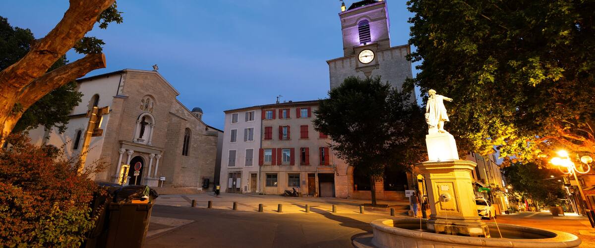A historic town square with a church, a clock tower, and a statue.