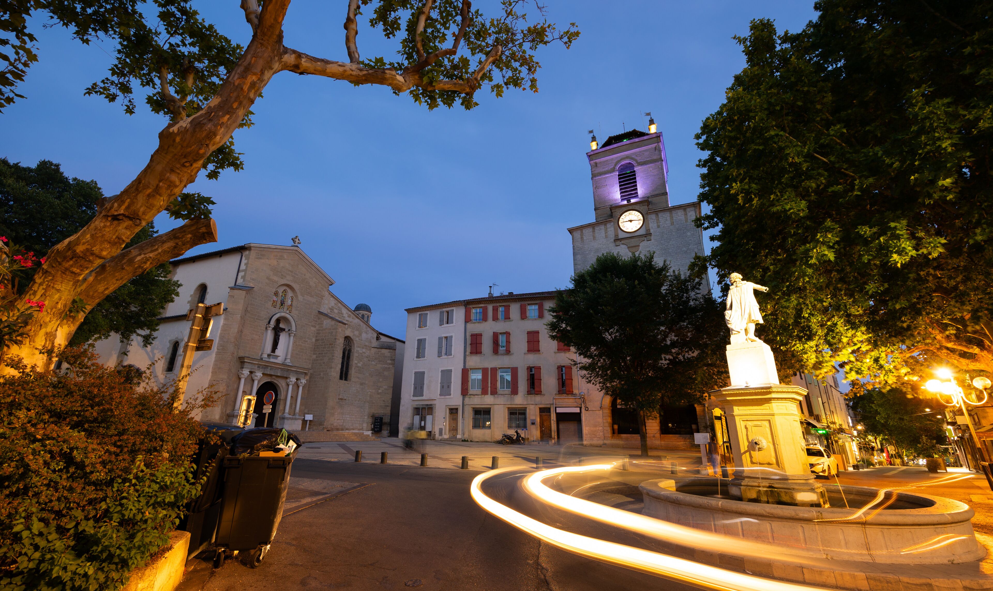 A historic town square with a clock tower, a statue, and a fountain.