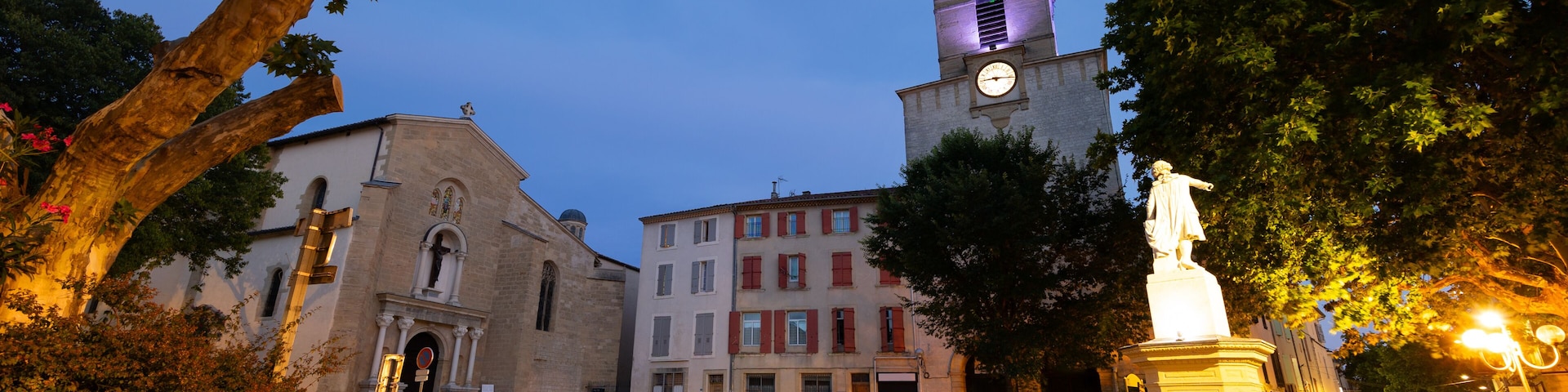 Una plaza histórica con una torre de reloj, una estatua y una fuente.