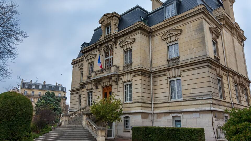 A historic building with a stone facade, a French flag, and a staircase leading to the entrance.