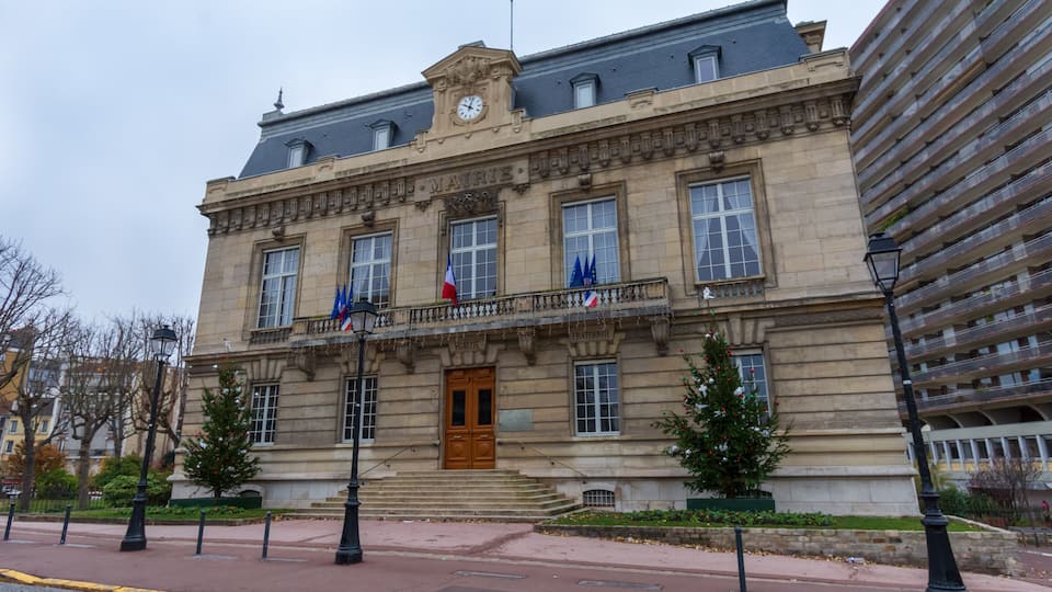 A historic building with a clock tower, French flags, and a balcony.