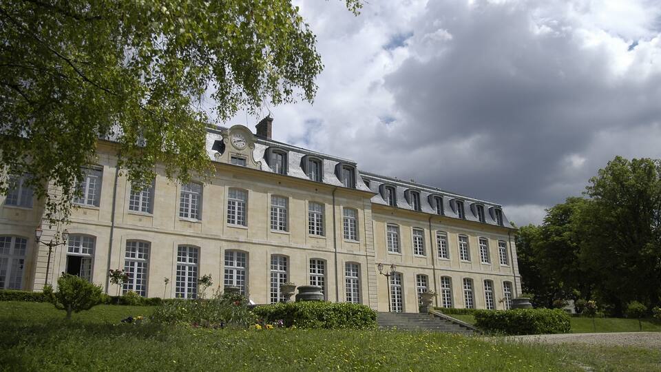 A large, historic building with symmetrical architecture, surrounded by lush greenery and a well-maintained garden.