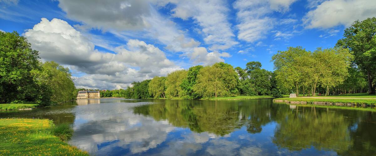 A calm river reflecting trees and a historic building.