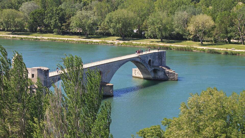 A stone bridge over a river, surrounded by trees and greenery.