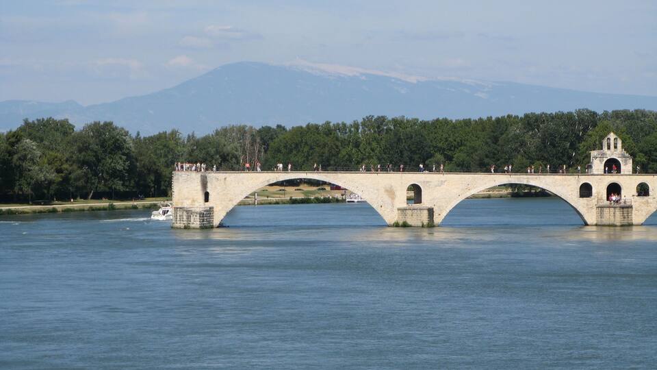 A stone bridge over a river with a forested mountain in the background.