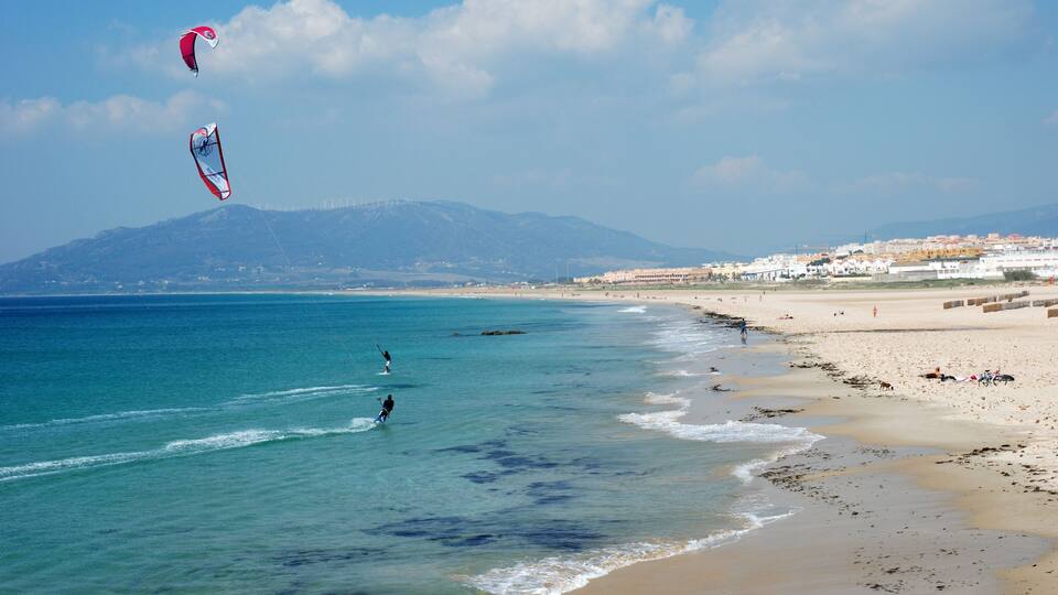 A beach with clear blue waters, a sandy shore, and a distant mountain range.