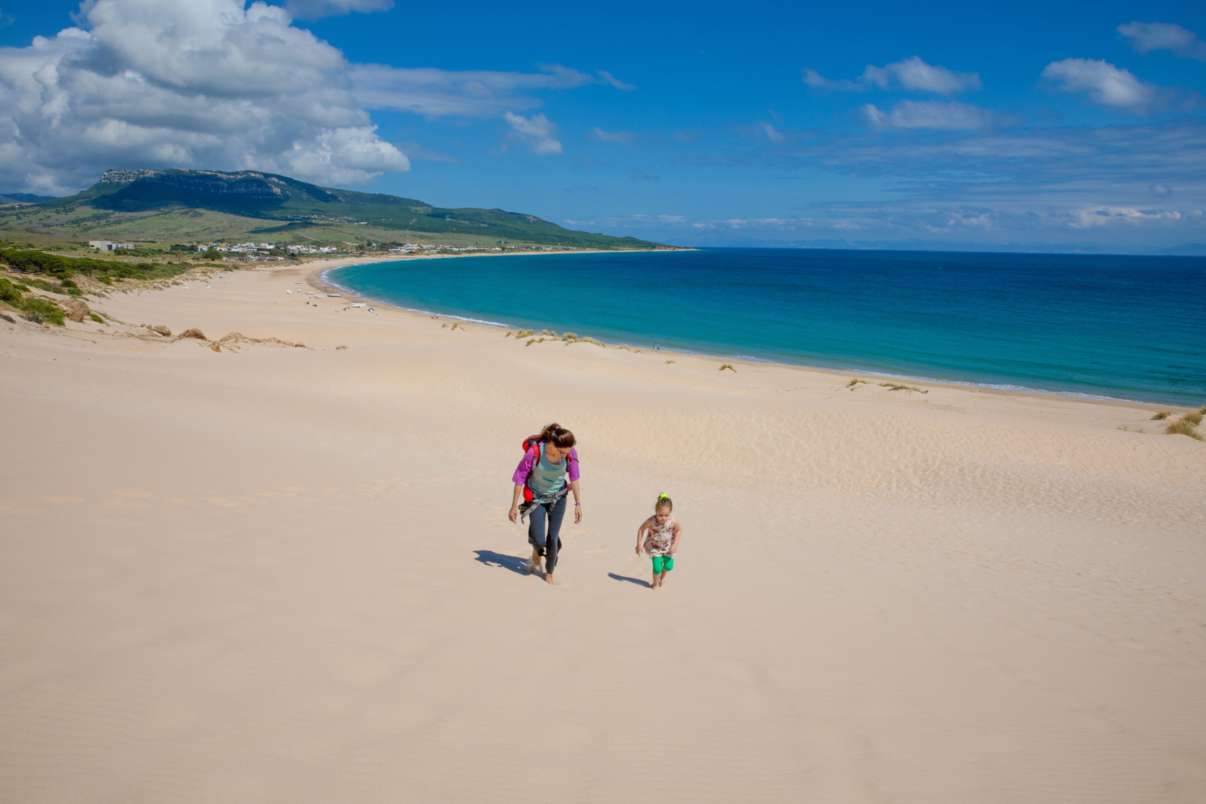 A sandy beach with a clear blue sea and a mountain in the background.
