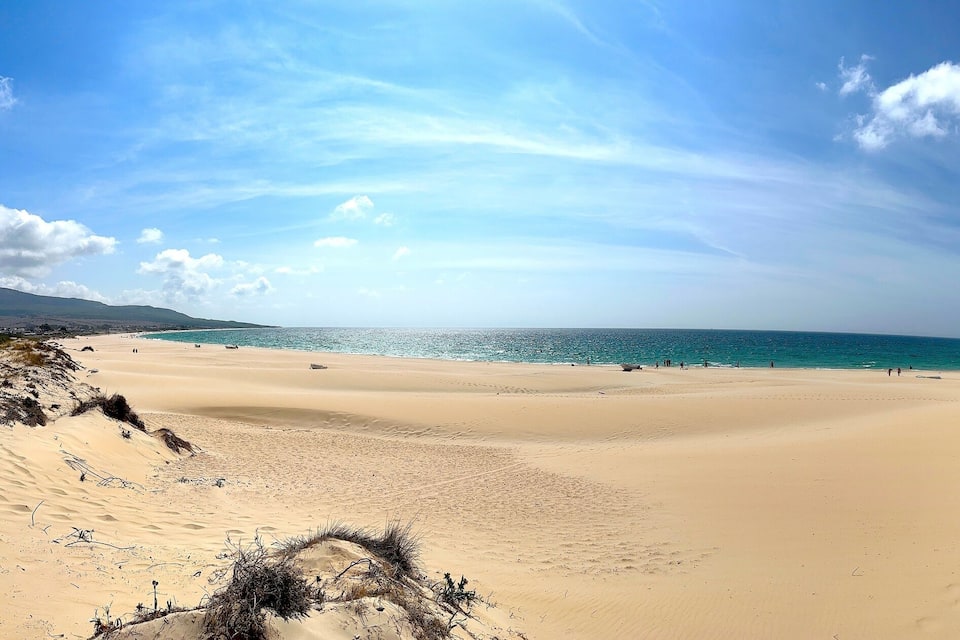 A wide sandy beach with a clear blue sky and calm sea.