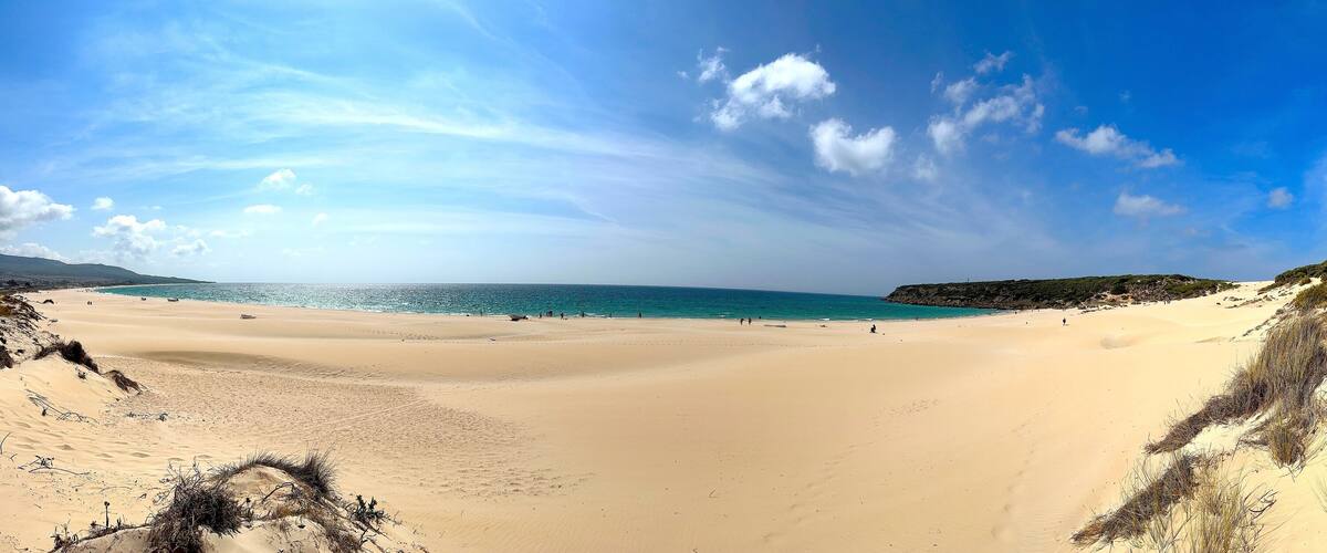 A wide sandy beach with a clear blue sky and calm sea.