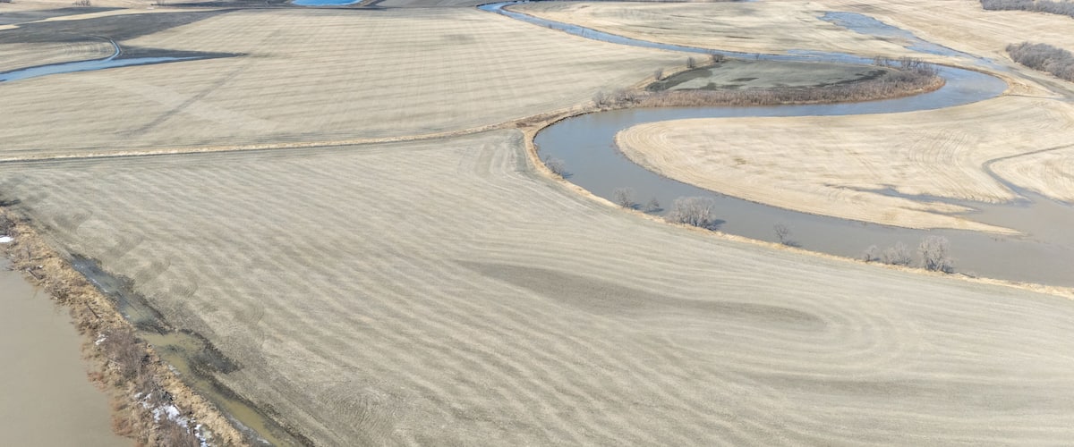 A river meandering through a flat landscape with fields and a small body of water.