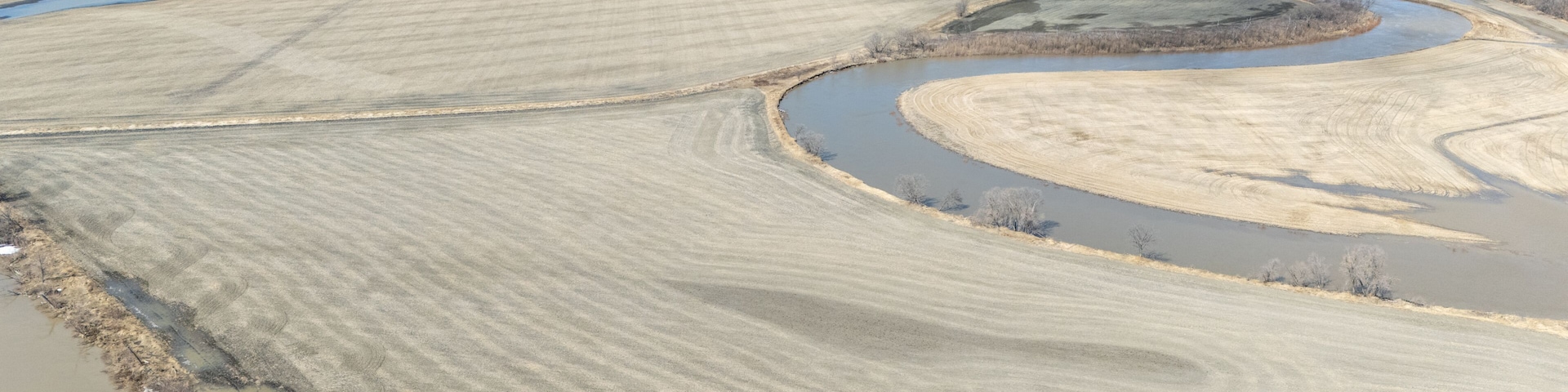 A river meandering through a flat landscape with fields and a small body of water.