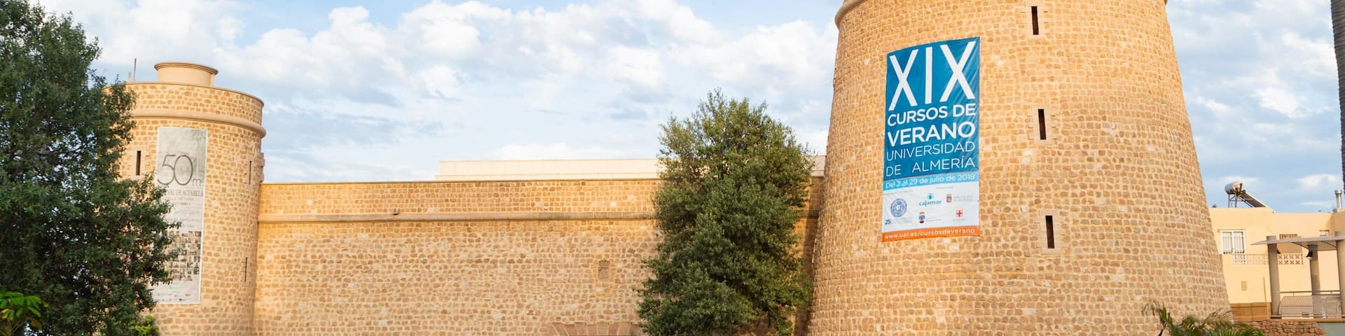 A historic stone building with a flag, a cannon, and lush greenery.