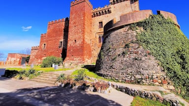 A historic castle with red brick walls, a stone tower, and a surrounding garden.