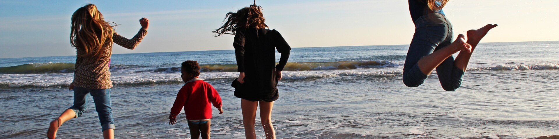 Una playa con olas, gente jugando y un cielo despejado.