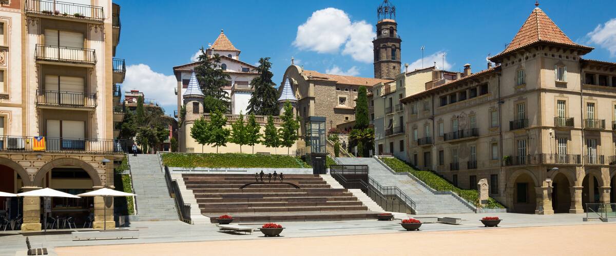 A historic square with a central staircase, surrounded by classical architecture and a clear blue sky.