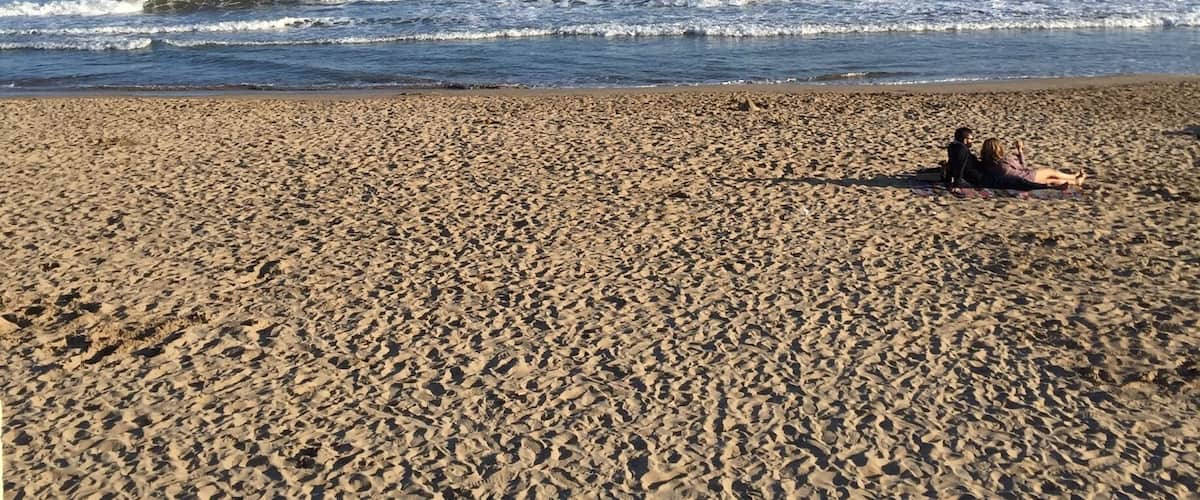 A sandy beach with waves crashing onto the shore and a clear blue sky.