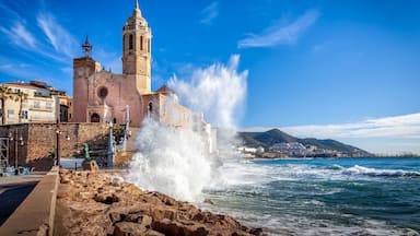 A coastal church with a bell tower, waves crashing against the rocks, and a clear blue sky.