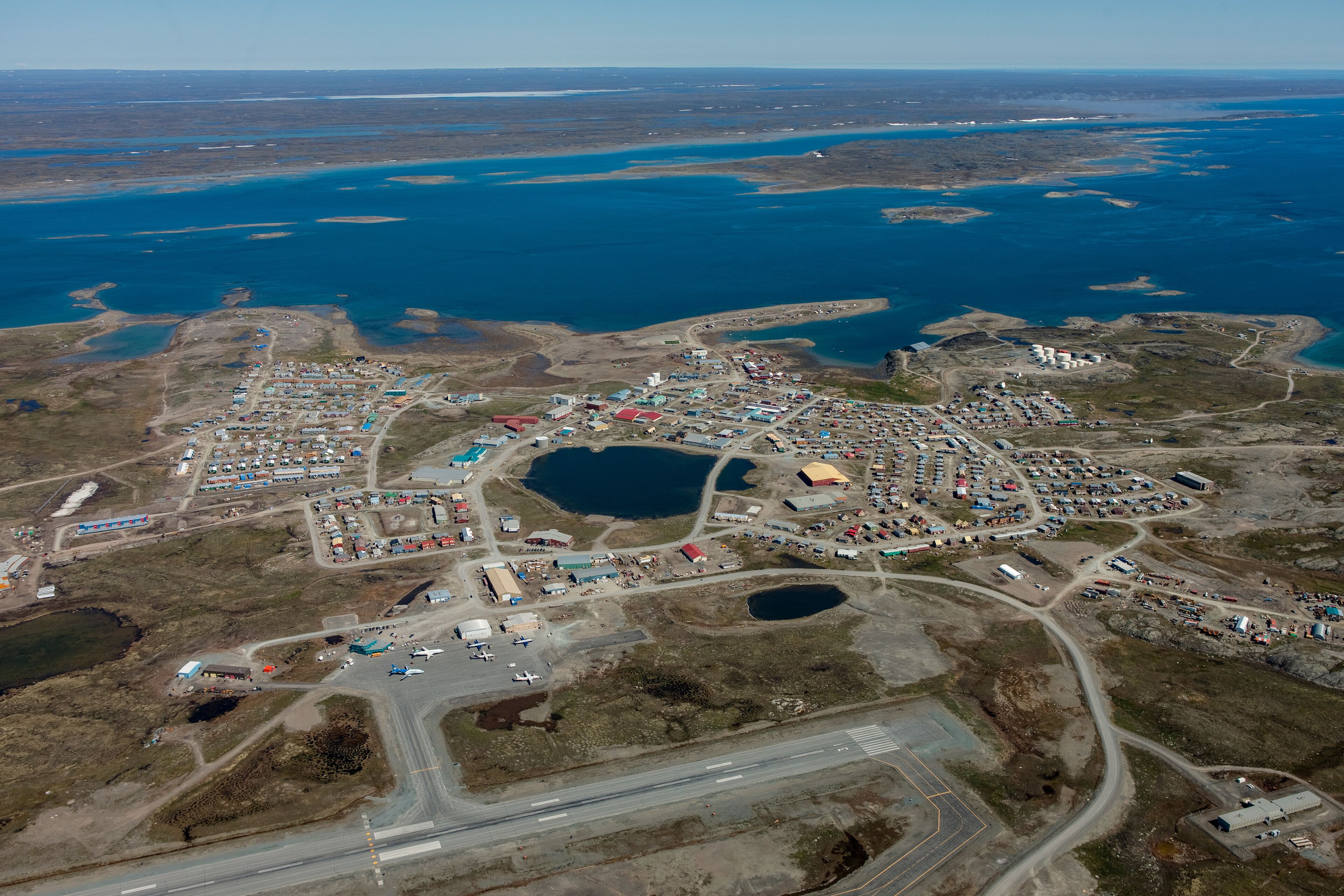 An aerial view of a coastal town with a harbor, several buildings, and a large body of water.
