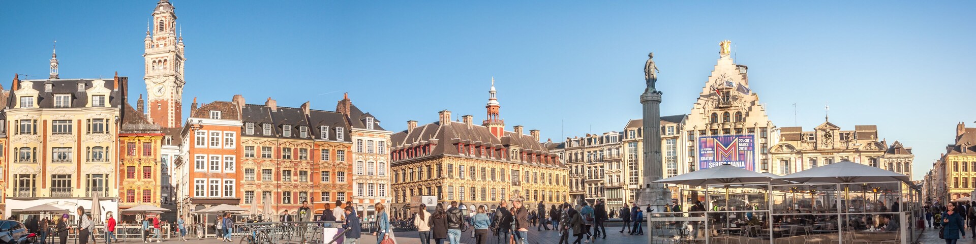 A historic square with ornate buildings, a prominent clock tower, and a statue.