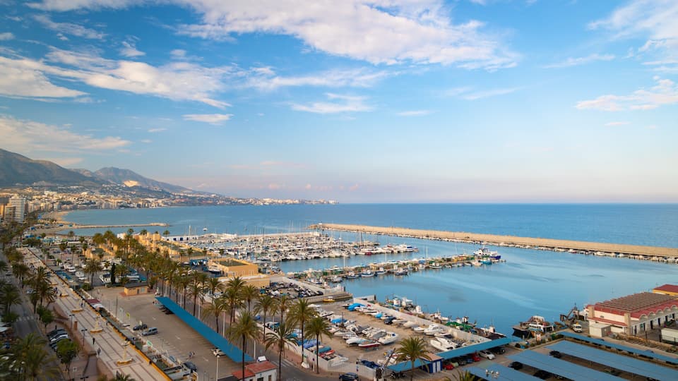 A coastal marina with boats, a beach, and a mountainous backdrop.