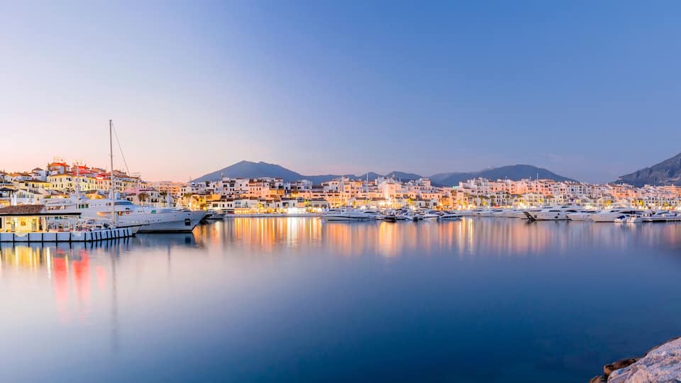 A coastal town with a marina, buildings, and a mountain in the background.