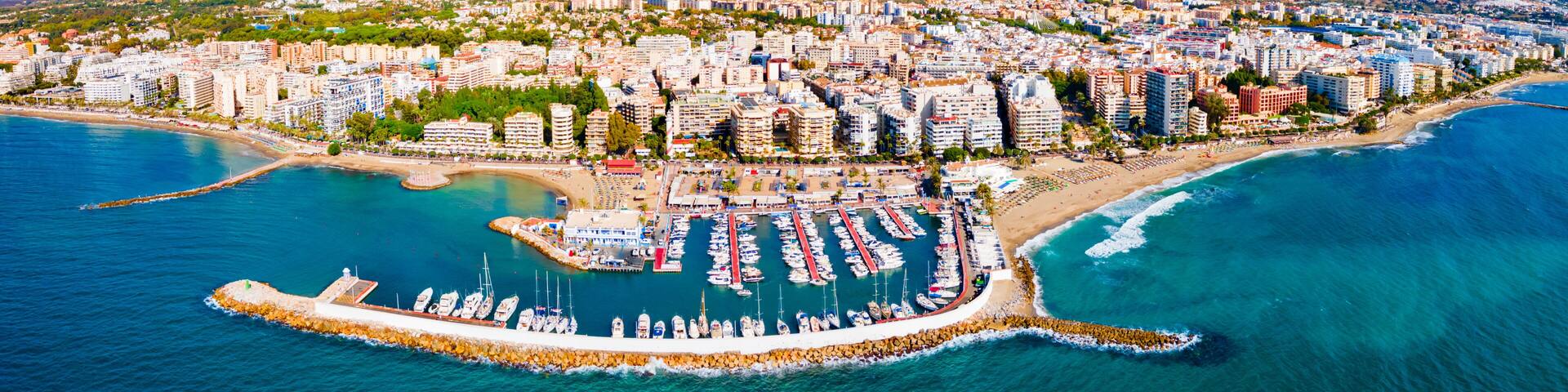 A coastal city with a marina, mountains in the background, and a clear sky.