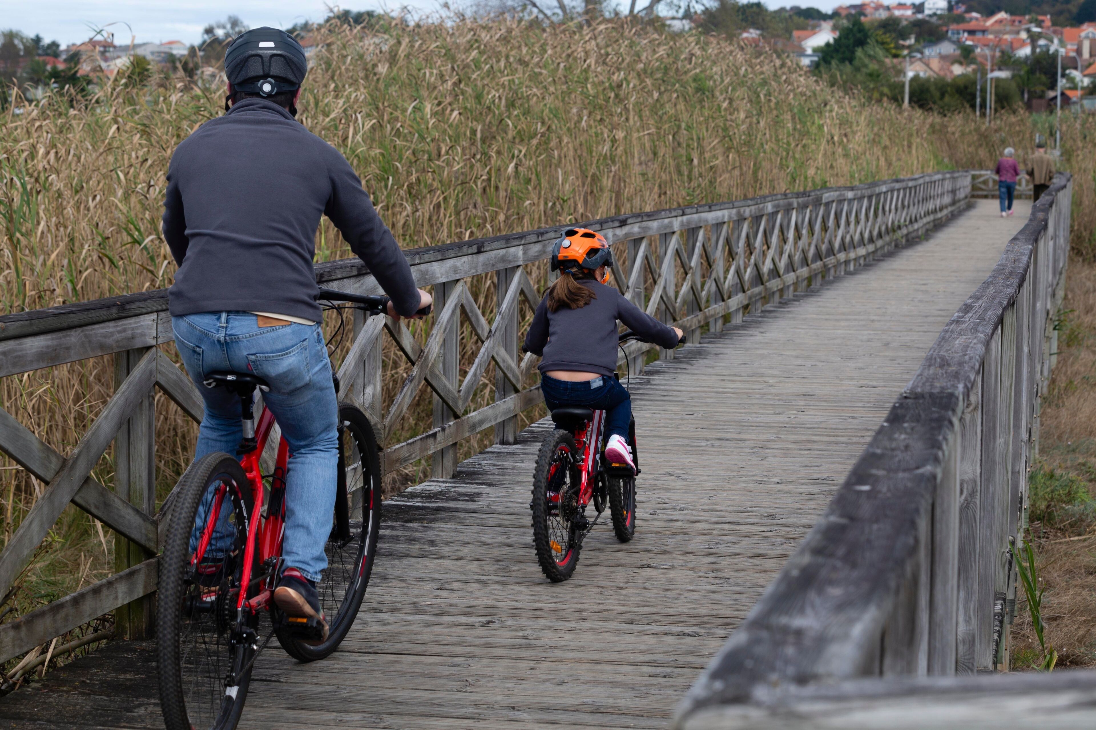 A father and his young son ride a bicycle along the wooden promenade of Panxon beach in Pontevedra
