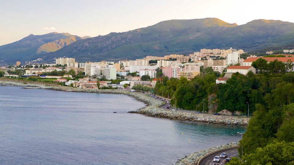 A coastal city with a rocky shoreline, a road along the coast, and mountains in the background.